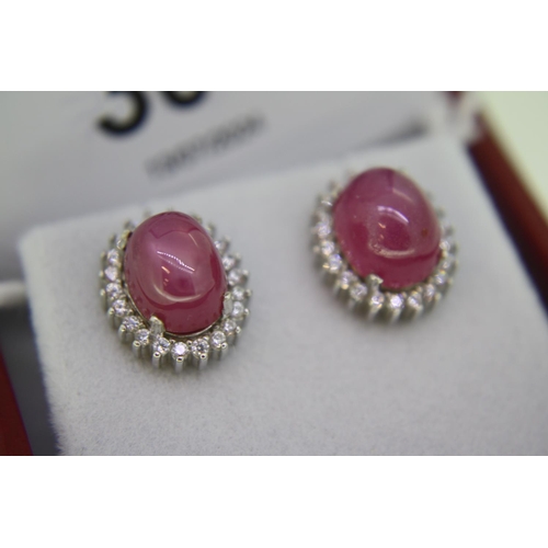 306 - Pair of treated cabochon ruby studs set in silver with white stone surround