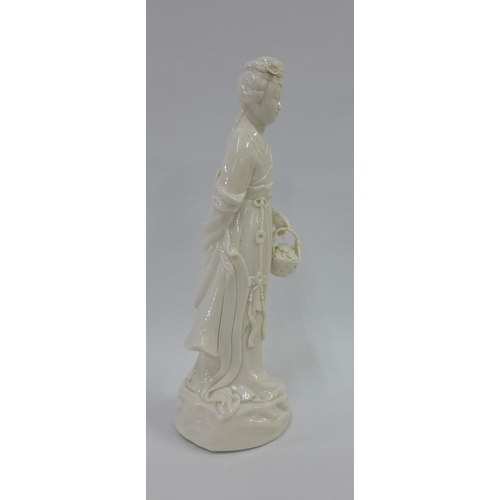 85 - Blanc de chine female figure, modelled standing carrying a basket of leaves, 26cm high