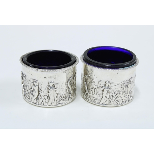 15 - Pair of Victorian silver salts, Birmingham 1899, circular form with repousse figures, glass liners a... 