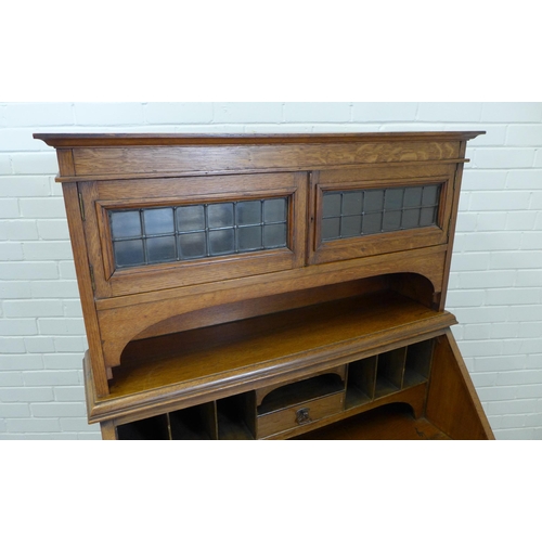 243 - An  early 20th century oak secretaire cabinet, the cornice top above two lead glazed panel doors and... 