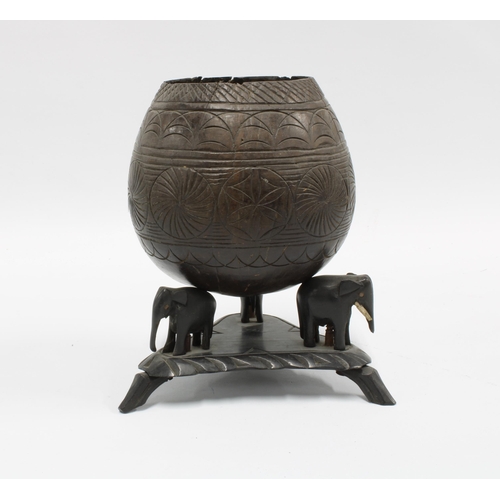 396 - Carved coconut shell on an ebonised stand with elephant supports, 17cm high