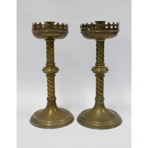 112 - A pair of brass Gothic Revival candlesticks with stylised drip trays, raised on barley twist columns... 