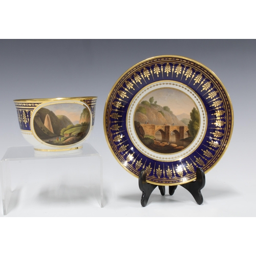 105 - A Barr Worcester teacup and saucer, with topographical scenes against a blue ground and gilt borders... 