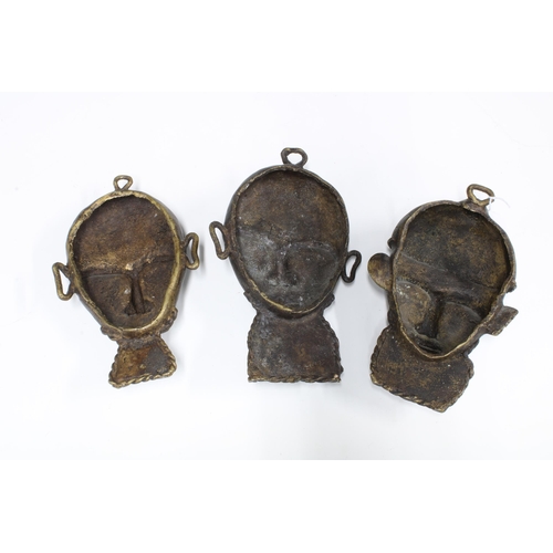 318 - Three Nigerian Benin type bronze wall masks, each with birds and lizards to the forehead, 20cm long ... 