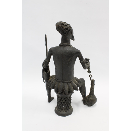 320 - African bronze figure, modelled seated and holding a long pipe and horn flask with a rope entwined v... 