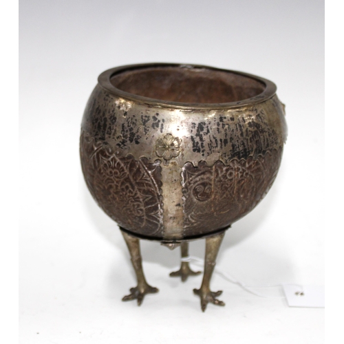 66 - South American white metal mounted and carved coconut cup, raised on three long legs with bird feet,... 