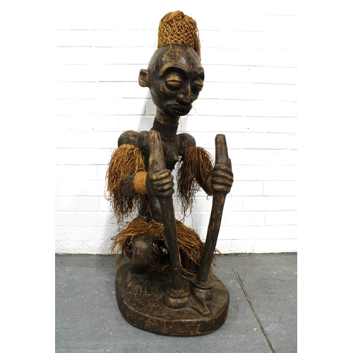 366 - African carved wooden figure, modelled seated with grass skirt and headress, 40 x 116cm.