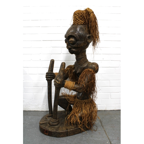 366 - African carved wooden figure, modelled seated with grass skirt and headress, 40 x 116cm.