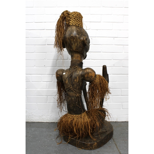 366 - African carved wooden figure, modelled seated with grass skirt and headress, 40 x 116cm.