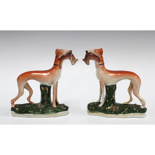 86 - A pair of Staffordshire greyhound figures, each modelled standing with a rabbit in their mouth (one ... 