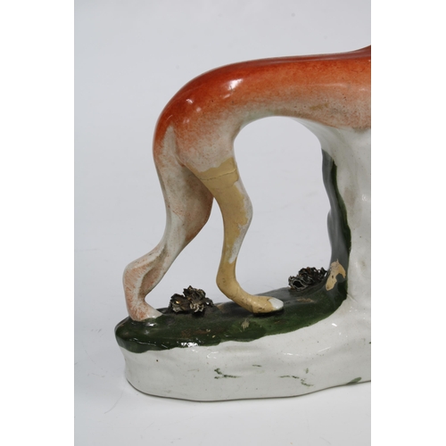 86 - A pair of Staffordshire greyhound figures, each modelled standing with a rabbit in their mouth (one ... 