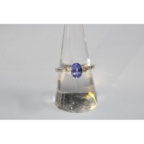 14 - 14ct white gold diamond and tanzanite dress ring, with an oval claw set tanzanite flanked by two bri... 