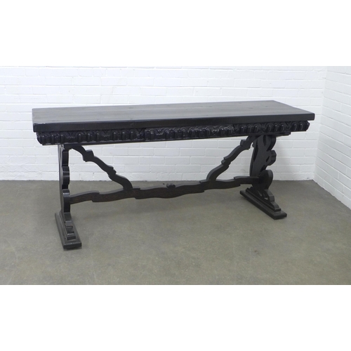 278 - An ebonised wooden table, long rectangular top with a carved frieze, on pierced side supports untied... 