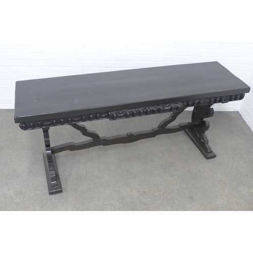 278 - An ebonised wooden table, long rectangular top with a carved frieze, on pierced side supports untied... 