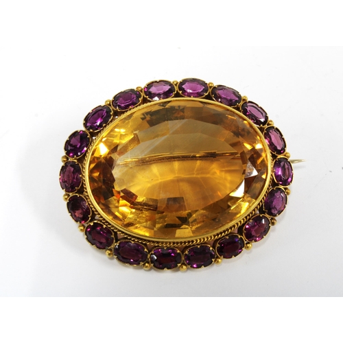 67 - A citrine and rhodolite brooch, set in unmarked yellow metal, with a large oval citrine within a sur... 