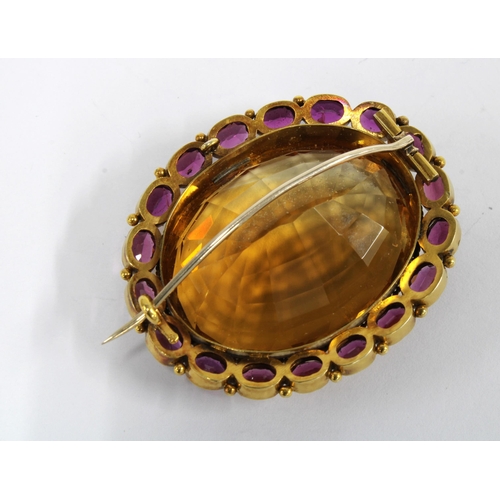 67 - A citrine and rhodolite brooch, set in unmarked yellow metal, with a large oval citrine within a sur... 