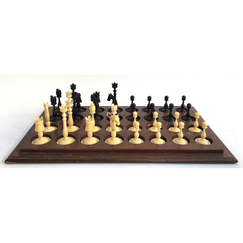 1052 - An antique carved ivory and ebony chess set, height of kings 8.1cm, set on wooden stand with cover