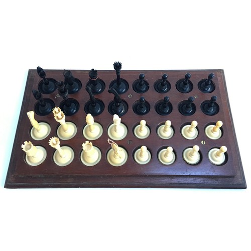 1052 - An antique carved ivory and ebony chess set, height of kings 8.1cm, set on wooden stand with cover