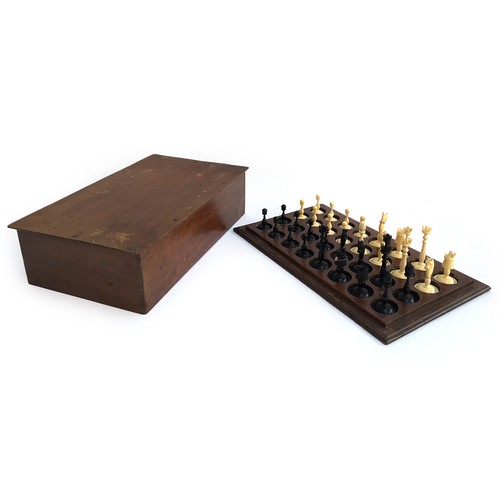 1052 - An antique carved ivory and ebony chess set, height of kings 8.1cm, set on wooden stand with cover