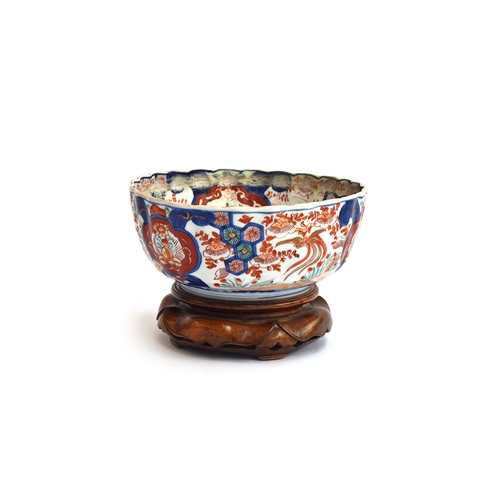 158 - An Imari bowl with scalloped edges and hand painted interior and surround detail, on carved hardwood... 