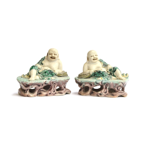 169 - A pair of famille verte biscuit porcelain Budai figures, with green underglaze robes, reclined upon ... 