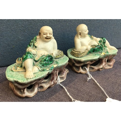 169 - A pair of famille verte biscuit porcelain Budai figures, with green underglaze robes, reclined upon ... 