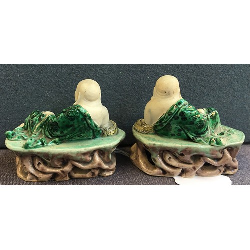 169 - A pair of famille verte biscuit porcelain Budai figures, with green underglaze robes, reclined upon ... 