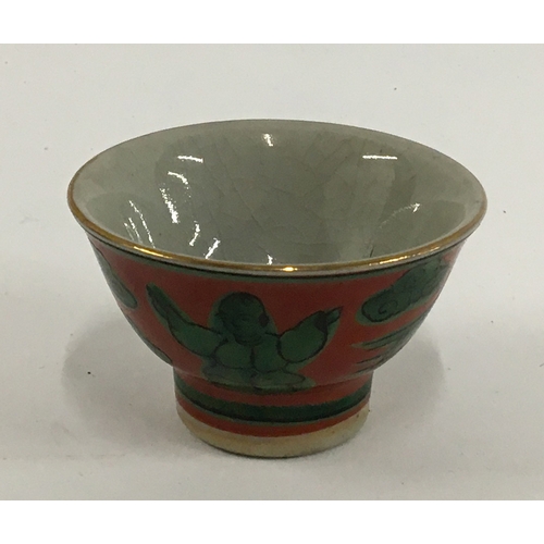 33 - A Japanese Yakimono sake cup, Guinomi Kutani ware, green Karako design on a red background, marks to... 