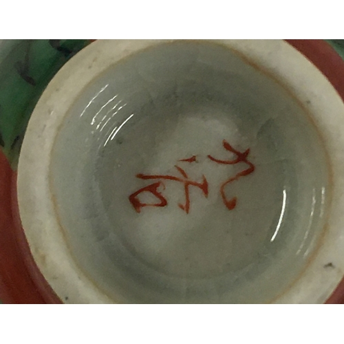 33 - A Japanese Yakimono sake cup, Guinomi Kutani ware, green Karako design on a red background, marks to... 