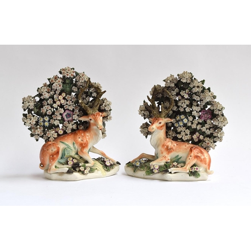 196 - A pair of 18th century Derby porcelain figures of recumbent stags, resting beneath flowering bocage,... 