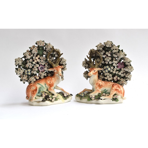 196 - A pair of 18th century Derby porcelain figures of recumbent stags, resting beneath flowering bocage,... 