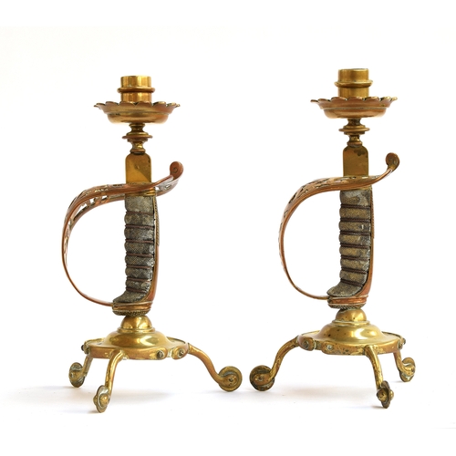 169 - A pair of brass candlesticks formed with Victorian sword hilts with shagreen and wire grips, cylindr... 