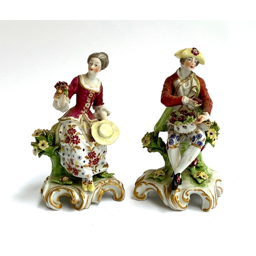 67 - A pair of continental figurines of a gentleman and lady seated upon tree stumps, floral encrusted, e... 