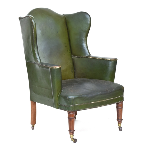 618 - A late Victorian wingback armchair, upholstered in green leather, on ring turned legs with brass can... 