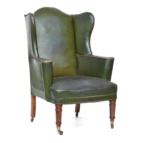 618 - A late Victorian wingback armchair, upholstered in green leather, on ring turned legs with brass can... 