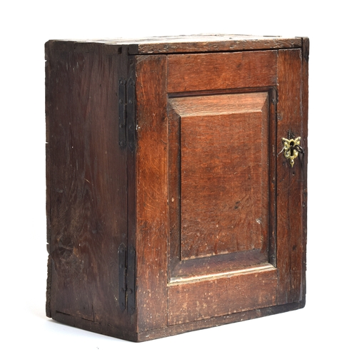 514 - A 17th century oak wall cupboard, single fielded panel door, opening to an arrangement of five shelv... 