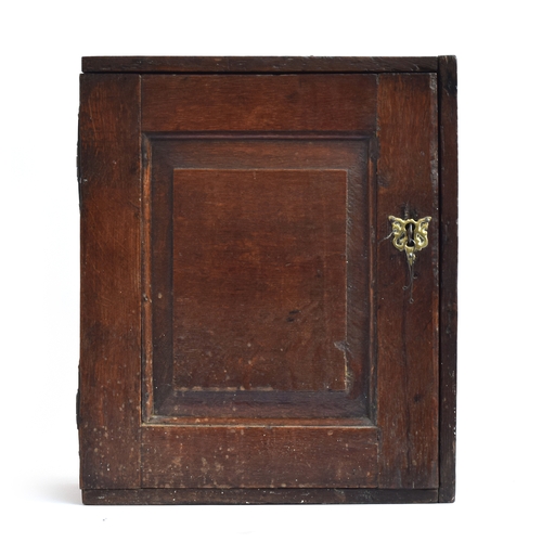 514 - A 17th century oak wall cupboard, single fielded panel door, opening to an arrangement of five shelv... 