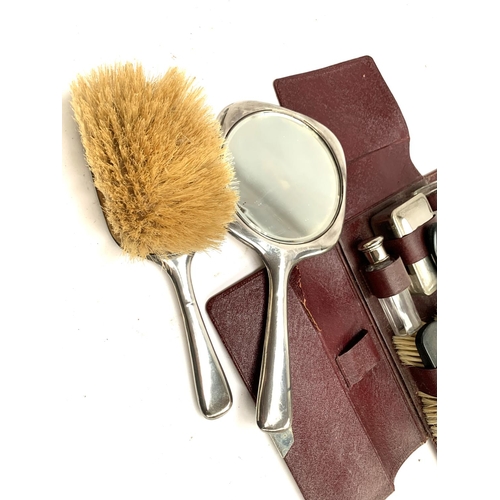 23 - A morocco leather vanity set, with ebonised brushes and looking glass and white metal topped bottles... 