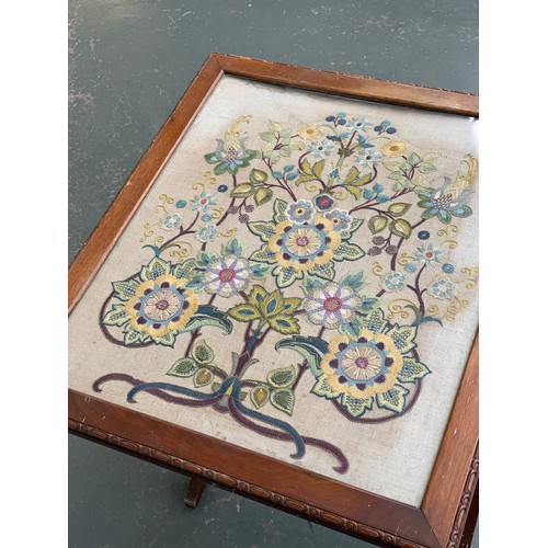 932 - A converting oak framed occasional table/fire screen, with glazed embroidered panel with floral deco... 