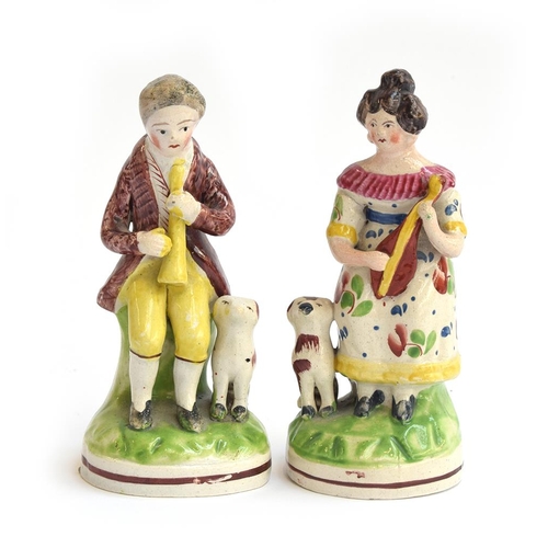 209 - A pair of Staffordshire figures of a man with a horn and a lady with a mandolin, each sitting on a g... 