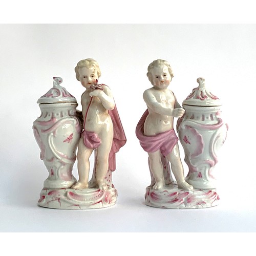 215A - A pair of Schierholz porcelain figures of putti holding an encrusted posy of flowers beside a lidded... 