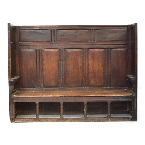 467 - An 18th century oak tavern settle, the panelled back and sides over a two plank pine seat, on four t... 