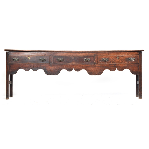 506 - An 18th century oak dresser base, three drawers over a shaped apron, on chamfered square section leg... 