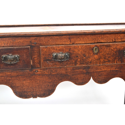 506 - An 18th century oak dresser base, three drawers over a shaped apron, on chamfered square section leg... 