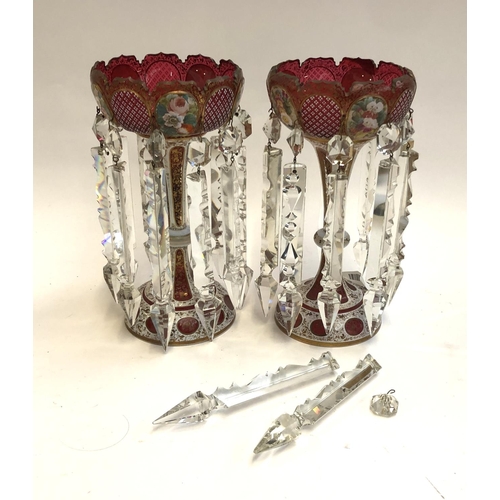 61 - A pair of cranberry and cut glass table lustres, with painted floral panels (one cut glass 'gem' mis... 