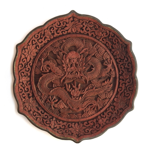 118 - A Chinese cinnabar lacquer lotus shaped dish depicting a dragon and a flaming pearl, surrounded by i... 