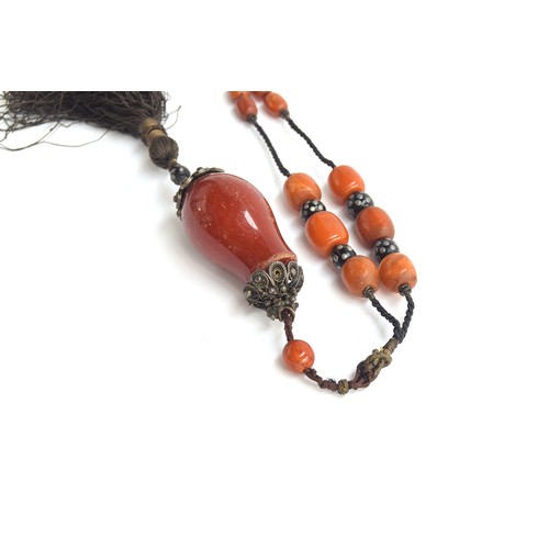 42 - An amber bead necklace, on knotted cord with silver studded coral beads, tassel hanging from a large... 