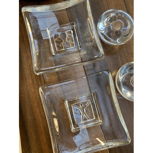 152 - Two Kosta Boda square glass dishes, each 10cm square, together with two glass candle stick holders, ... 