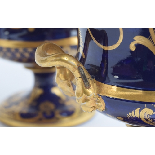 214 - A pair of 19th century twin handled porcelain urns, each with hand painted floral panel on a cobalt ... 