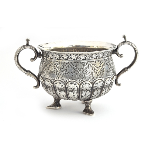 105 - An Indian silver twin handled sugar bowl, the half gadrooned body allover chased with foliate design... 